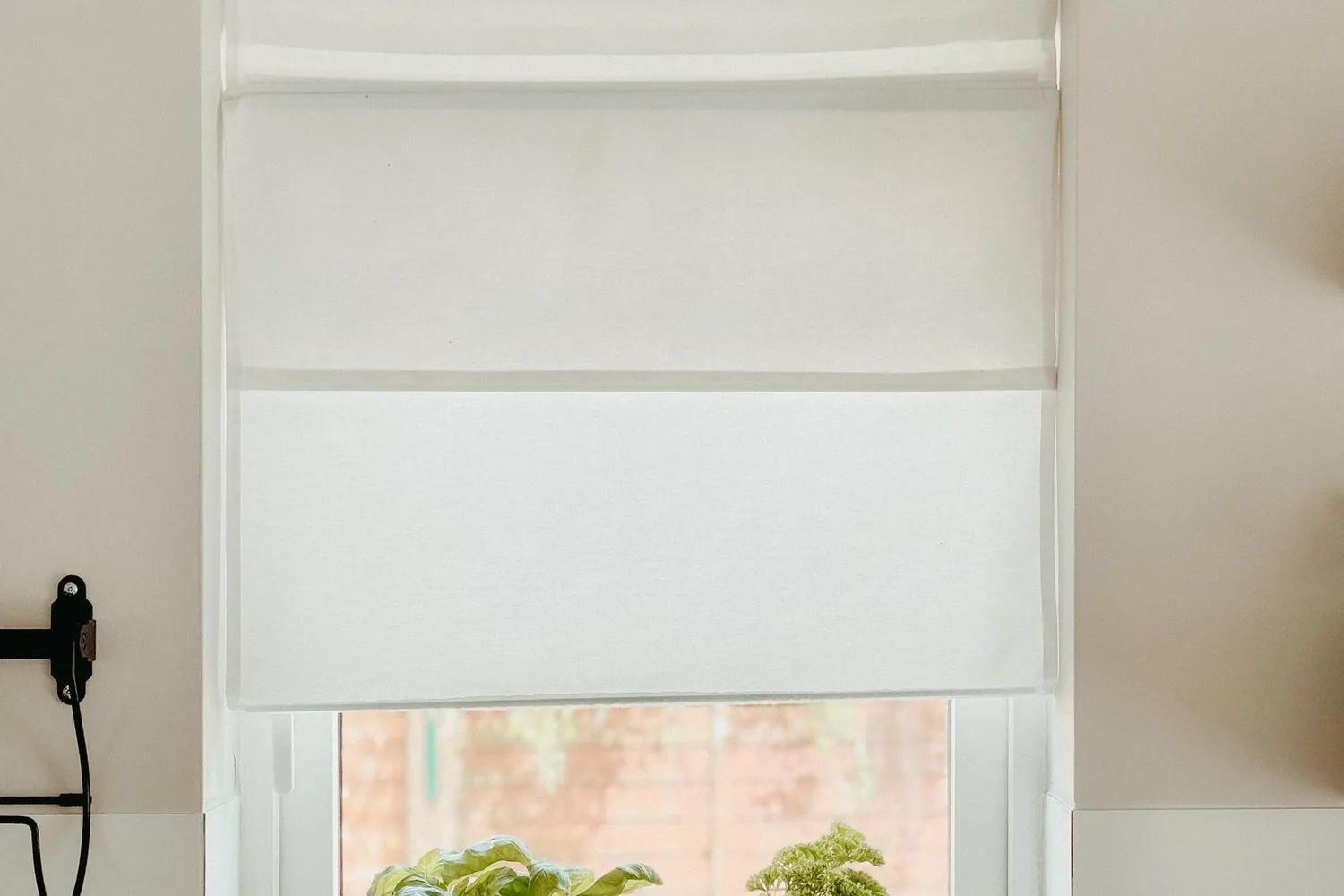 White roller blind half lowered in a bright kitchen window