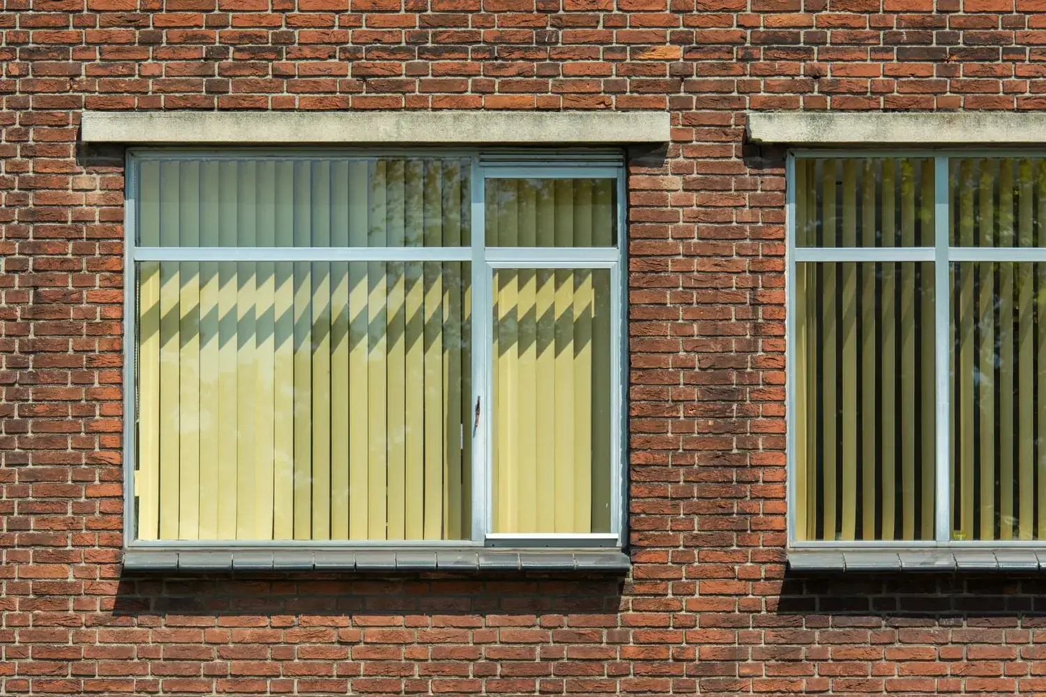 Vertical blinds behind large windows in a red brick building